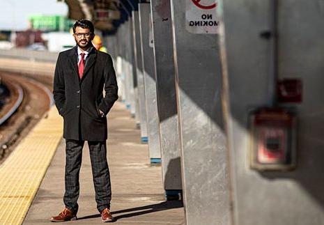 A man in a suit stands with his hands in his pockets on an elevated train platform.